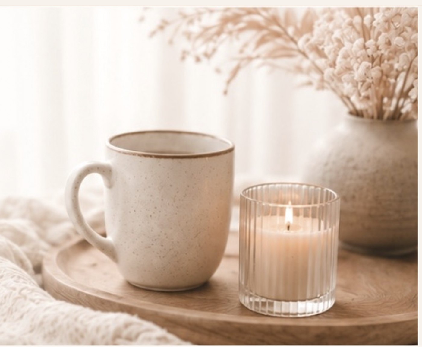 Tasse und Kerze auf einem Holztablett vor hellen Trockengräsern.